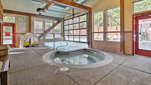 A hot tub in a room with large windows, wooden beams, and a door with a 'Please Use City Pool' sign.