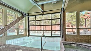 An indoor swimming pool with clear glass walls, a metal ladder, and a view of the outside.