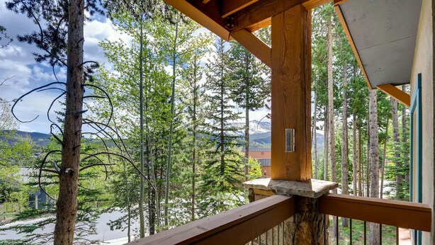A wooden balcony with a stone ledge, overlooking a forested area with tall trees and a distant mountain range.