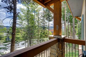 Een houten balkon met een stenen rand, met uitzicht op een bebost gebied met hoge bomen en een bergketen in de verte.