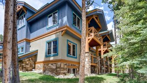 A multi-story log cabin with stone foundation, large windows, and a wooden deck.