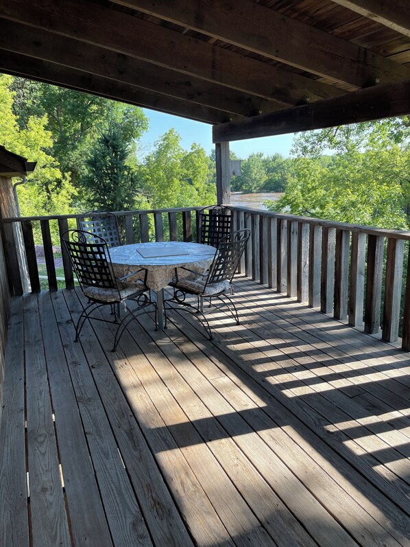 A wooden deck with a table and chairs, overlooking a river and trees.