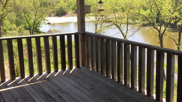 Una terraza de madera con barandilla que da a un río y abundante vegetación.