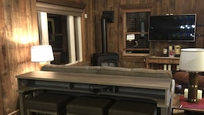 Un interior de madera con una zona de bar, un televisor y un ventanal.