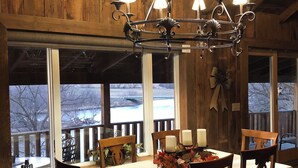 Un comedor con candelabro, paredes de madera y amplios ventanales con vistas a un paisaje nevado.