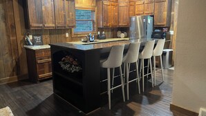 Una cocina moderna con armarios de madera, un refrigerador de acero inoxidable, una barra con taburetes e isla integrada con pileta.
