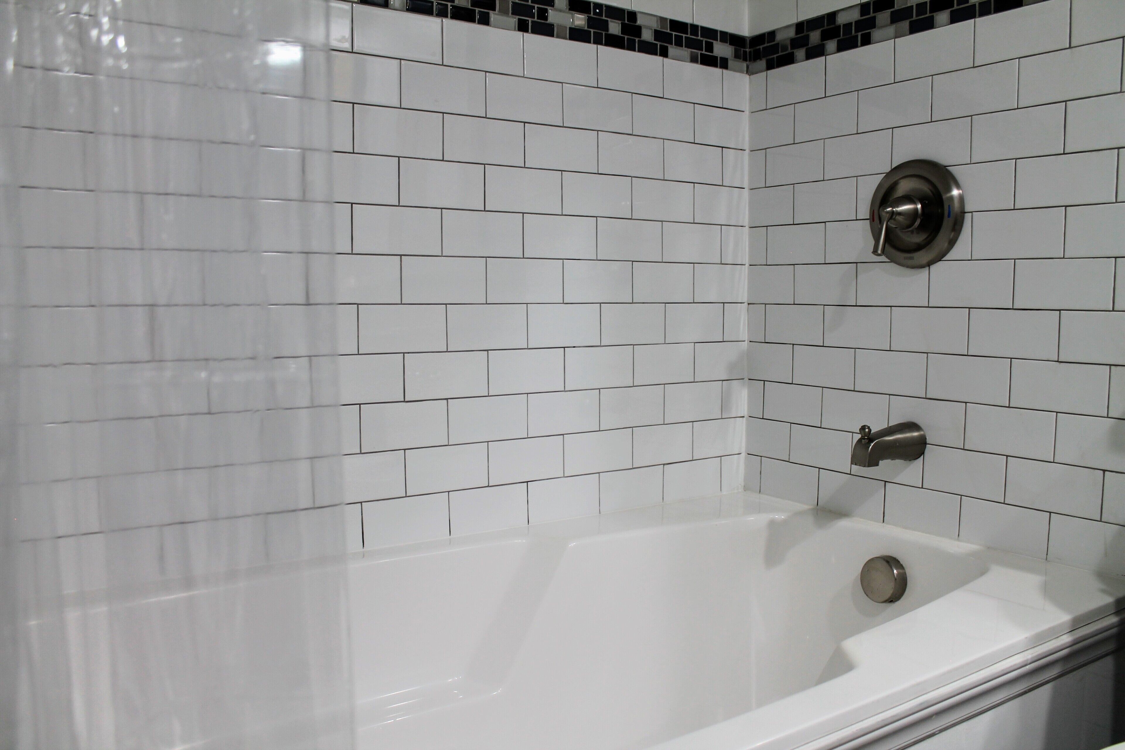 Une salle de bain avec des carreaux de céramique blancs rectangulaires, une baignoire blanche et un robinet argenté.