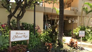 Señal de bienvenida a Maui Kai, zona de carga para registro de huéspedes y entrada del edificio con galería techada y jardines tropicales.