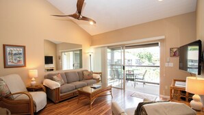 Ein geräumiges Wohnzimmer mit Holzboden, einer Couch, einem Sessel, einem Couchtisch und einem Deckenventilator.