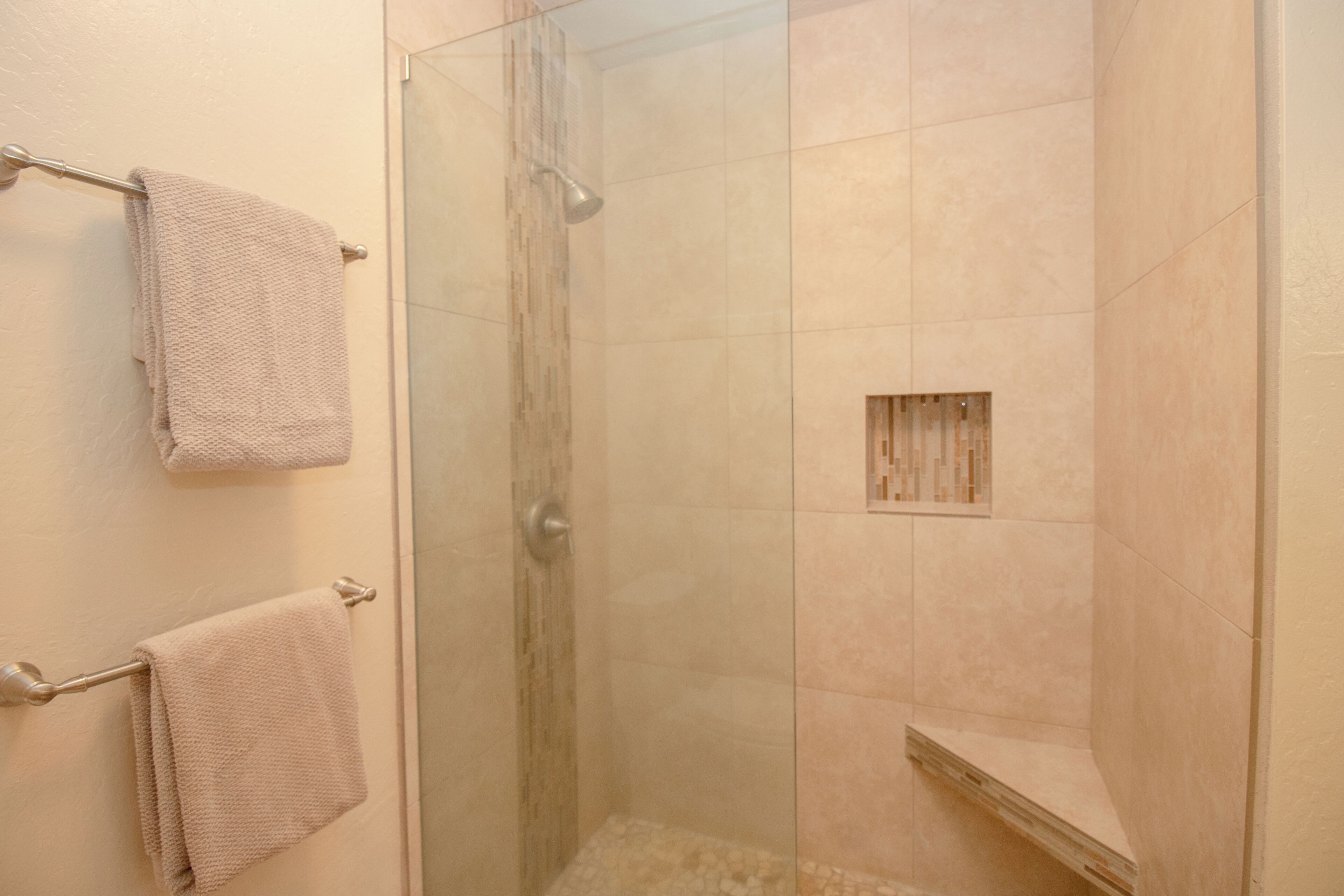 A glass-enclosed shower with beige tiles and a small shelf.