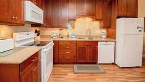 Una cocina con armarios de madera, microondas, estufa, lavavajillas y refrigerador.