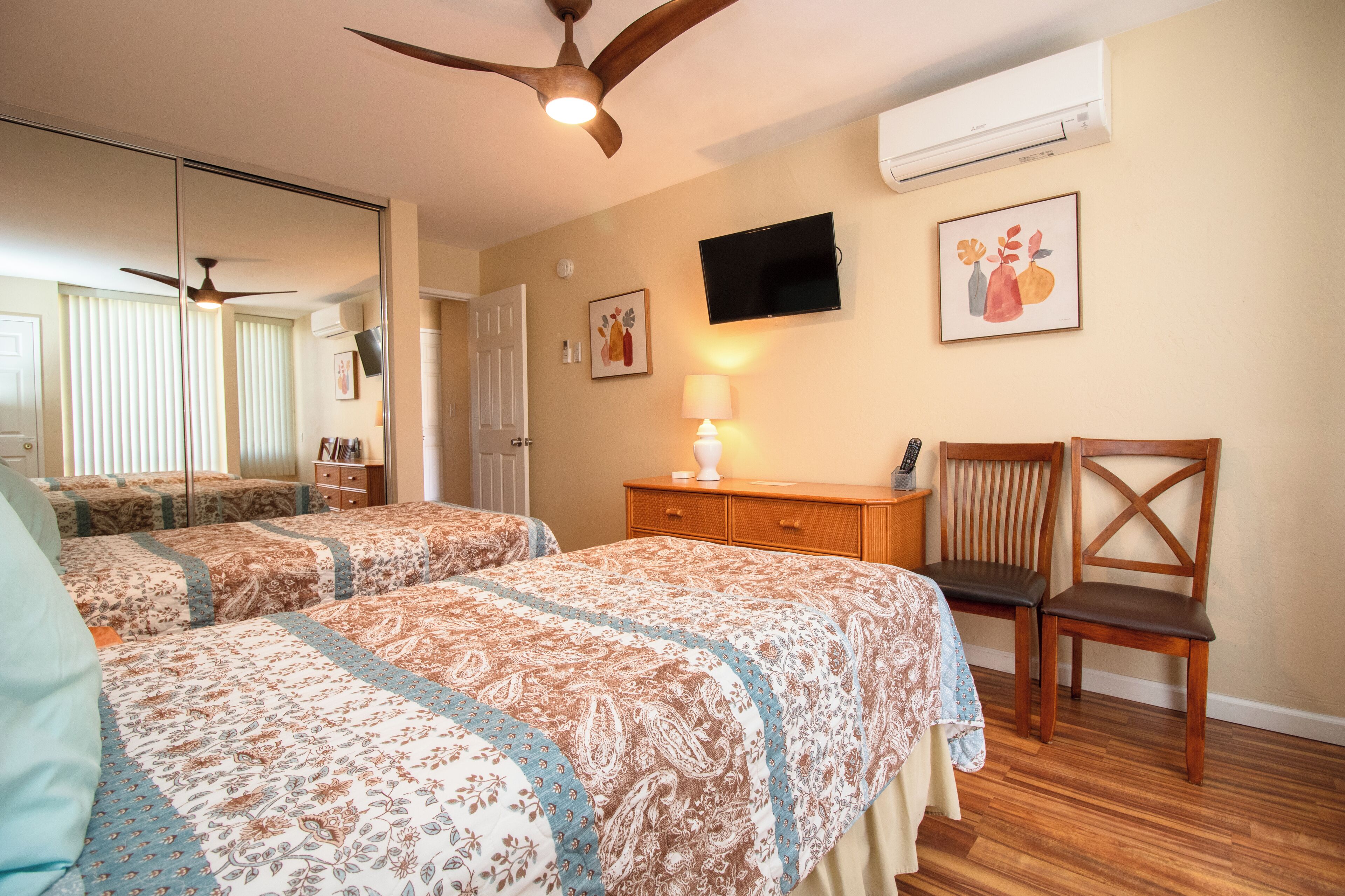 A bedroom with two beds, a ceiling fan, an air conditioner, a TV, and a wooden chair.