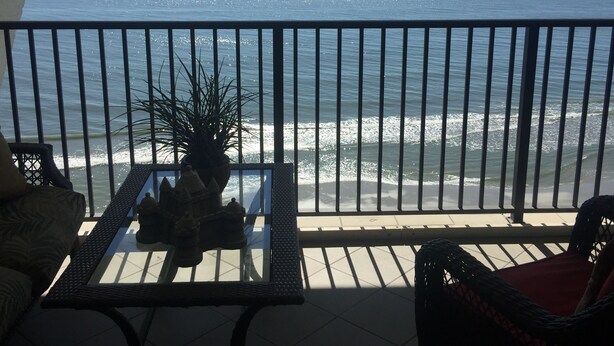 A balcony with a view of the ocean, a table with a plant and decorative items, and wicker furniture.