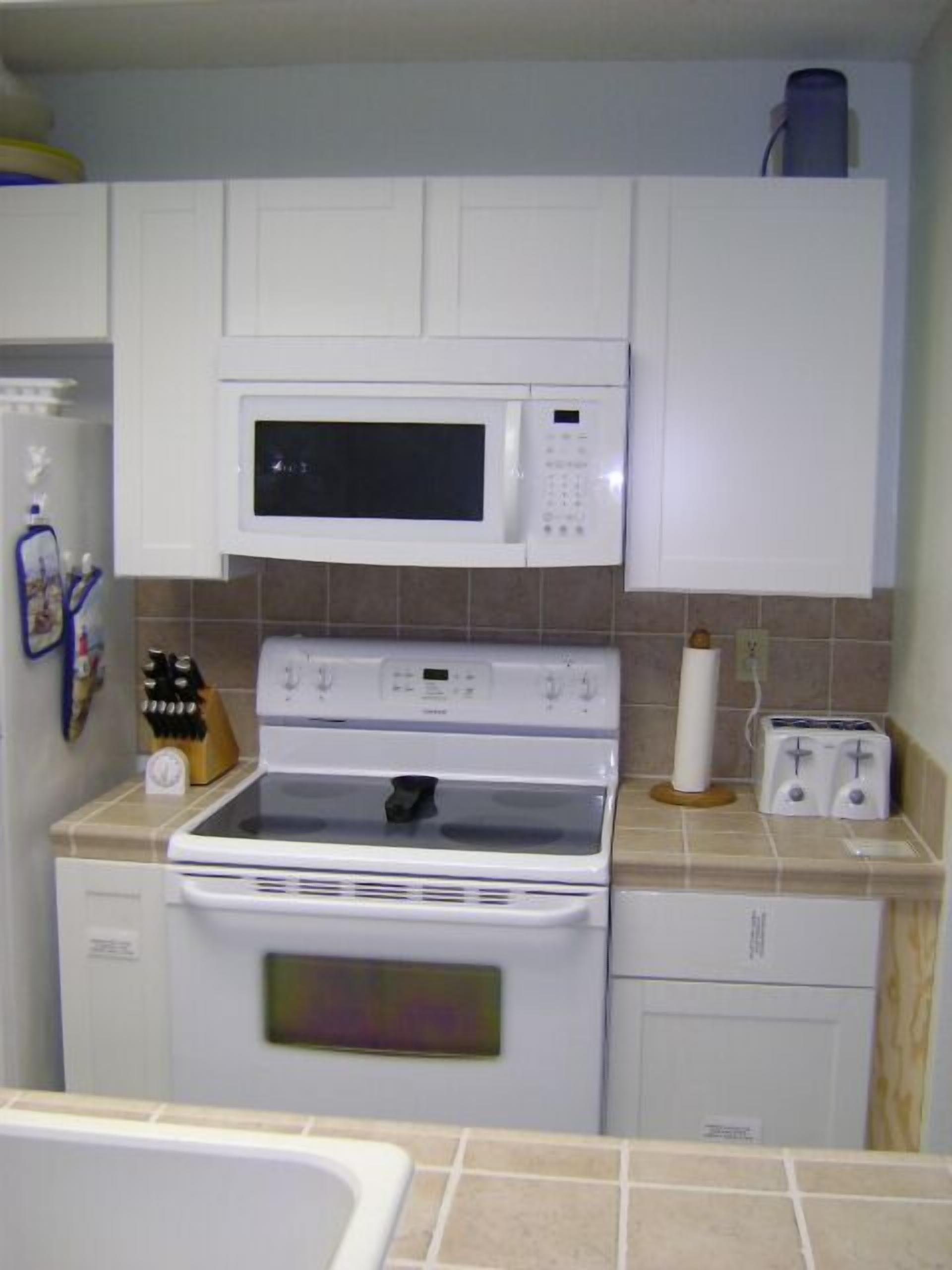 A kitchen with white cabinets, a microwave, an oven, a toaster, and a sink.