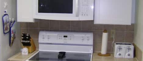 A kitchen with white cabinets, a microwave, an oven, a toaster, and a sink.