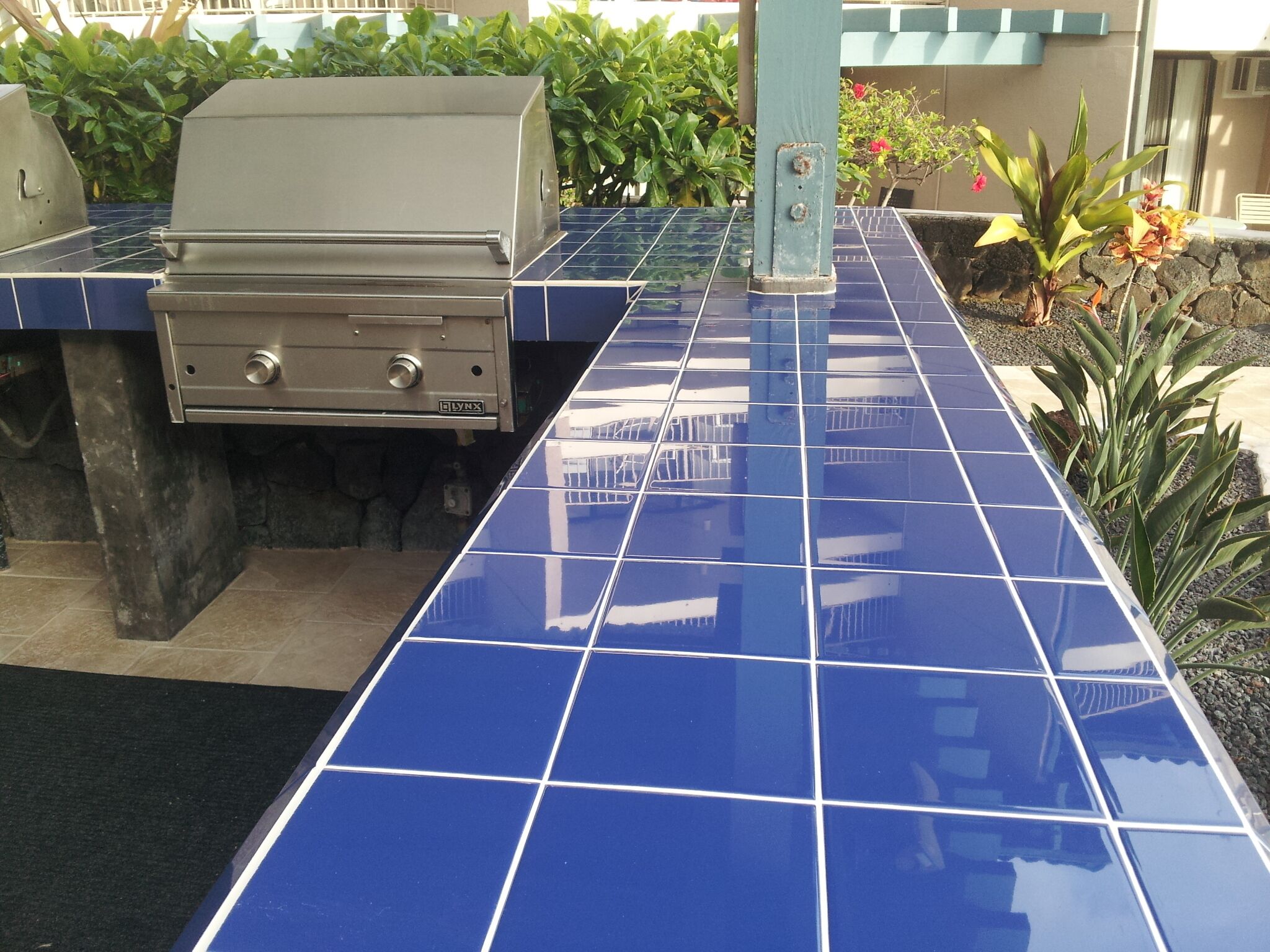 A patio area with a grill and blue-tiled flooring.
