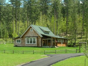 A rustic log cabin with a green roof, surrounded by a wooden fence and a paved driveway. - Little Elk Cottage in Scenic Vanocker Canyon - Blue Skies and Meadow Views! (Nemo)