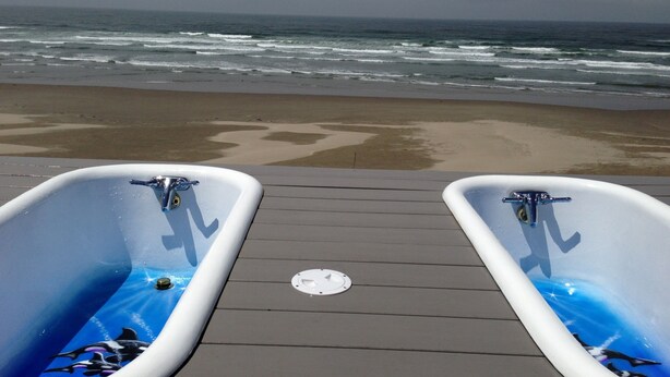 Two white bathtubs with blue ocean-themed designs on a wooden deck overlooking the ocean. - Ocean Front Home in the Heart of Newport! (Newport)