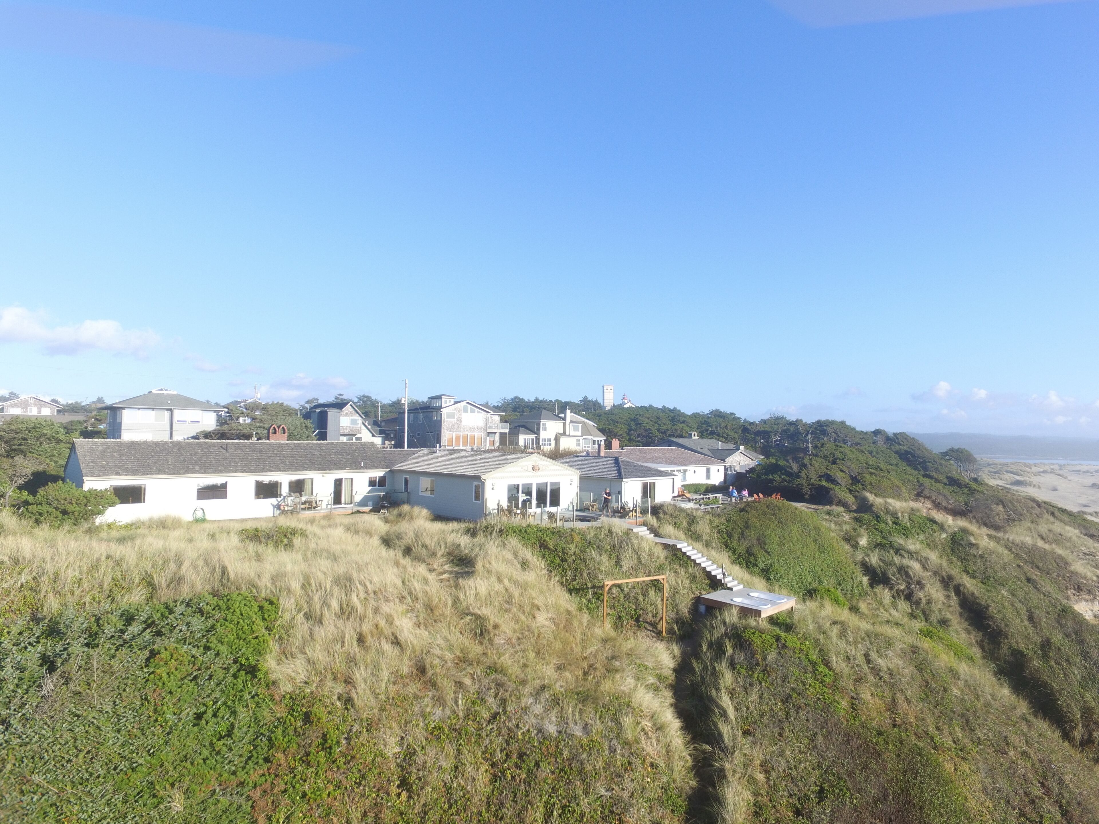 A coastal house with a prominent staircase leading to the entrance, surrounded by grassy terrain and overlooking the beach.