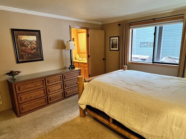 A bedroom with a bed, a dresser, a lamp, and a window with a view of the outside. - Large Great Room-3 Master Suites-Hot Tub-Backs up to the Forest-Pet Friendly (Sunriver)