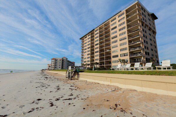 A beachfront hotel with multiple floors, balconies, and a sandy beach in the foreground.