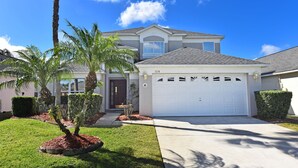 A two-story house with a garage, a well-maintained lawn, and a palm tree. - South facing pool,spa, communal pool, interior games room, Wifi, monitored alarm (Kissimmee)