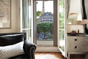 Una habitación con vistas a un edificio histórico, un balcón con barandillas de hierro decorativo, un sillón de cuero negro y una lámpara antigua sobre una cómoda.