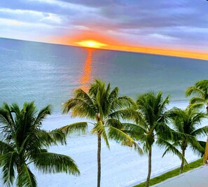 Een strand met palmbomen en een zonsondergang boven de oceaan.