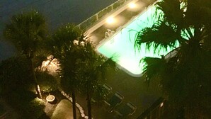 Vista noturna de uma praia com piscina e palmeiras.