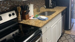 Une cuisine avec des meubles blancs, un four à micro-ondes en acier inoxydable, une cuisinière, un évier et un réfrigérateur.