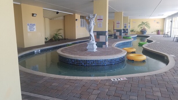 Un espace piscine agrémenté d’une statue, comprenant plusieurs bassins et des panneaux indiquant l’absence de maître-nageur.