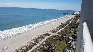 Une plage avec une jetée qui s’avance dans l’océan, un sentier sablonneux et quelques plantes.