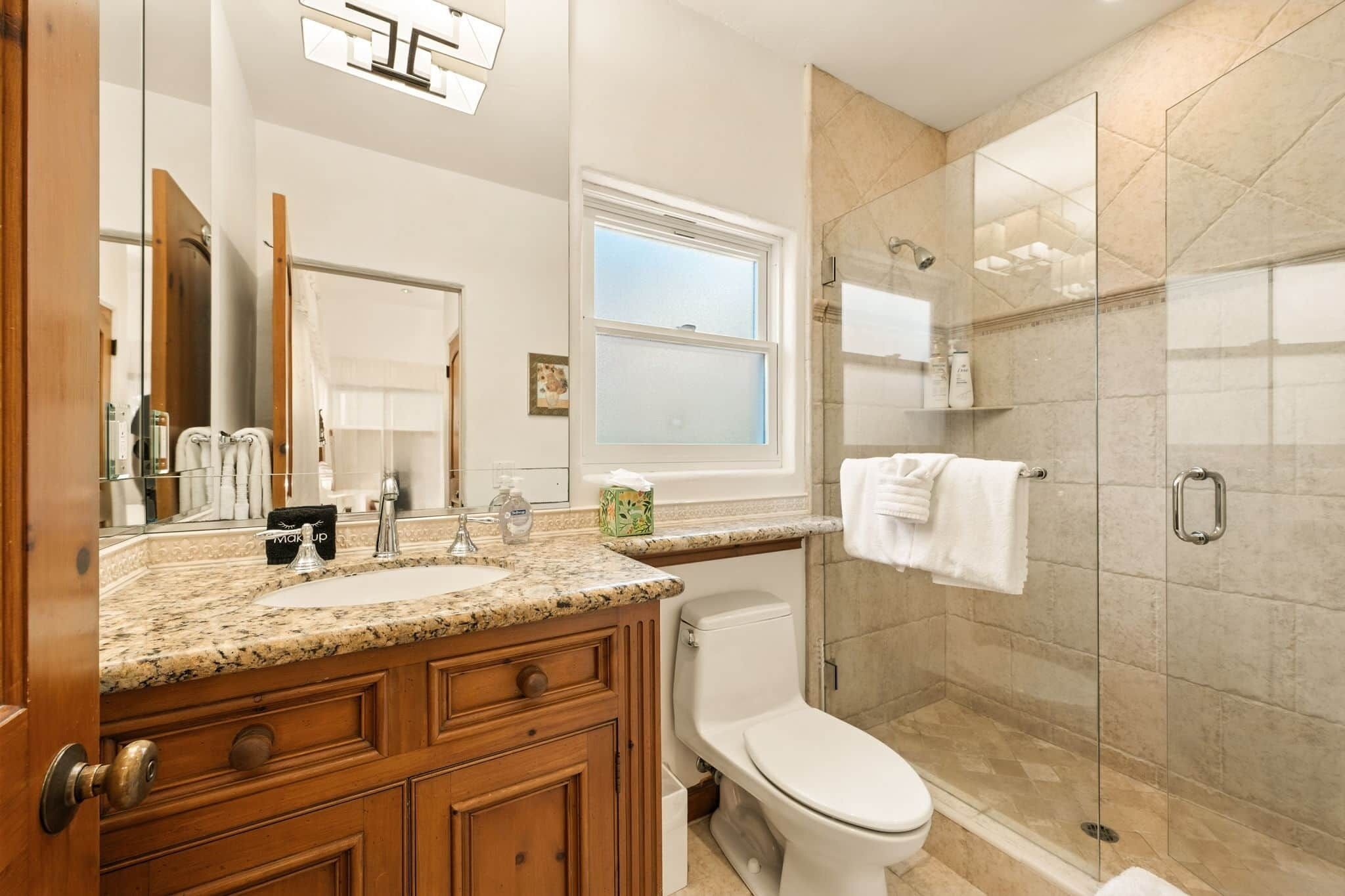 Une salle de bain moderne avec un lavabo sur un plan de travail en granit, des toilettes, une douche à parois de verre et un grand miroir.