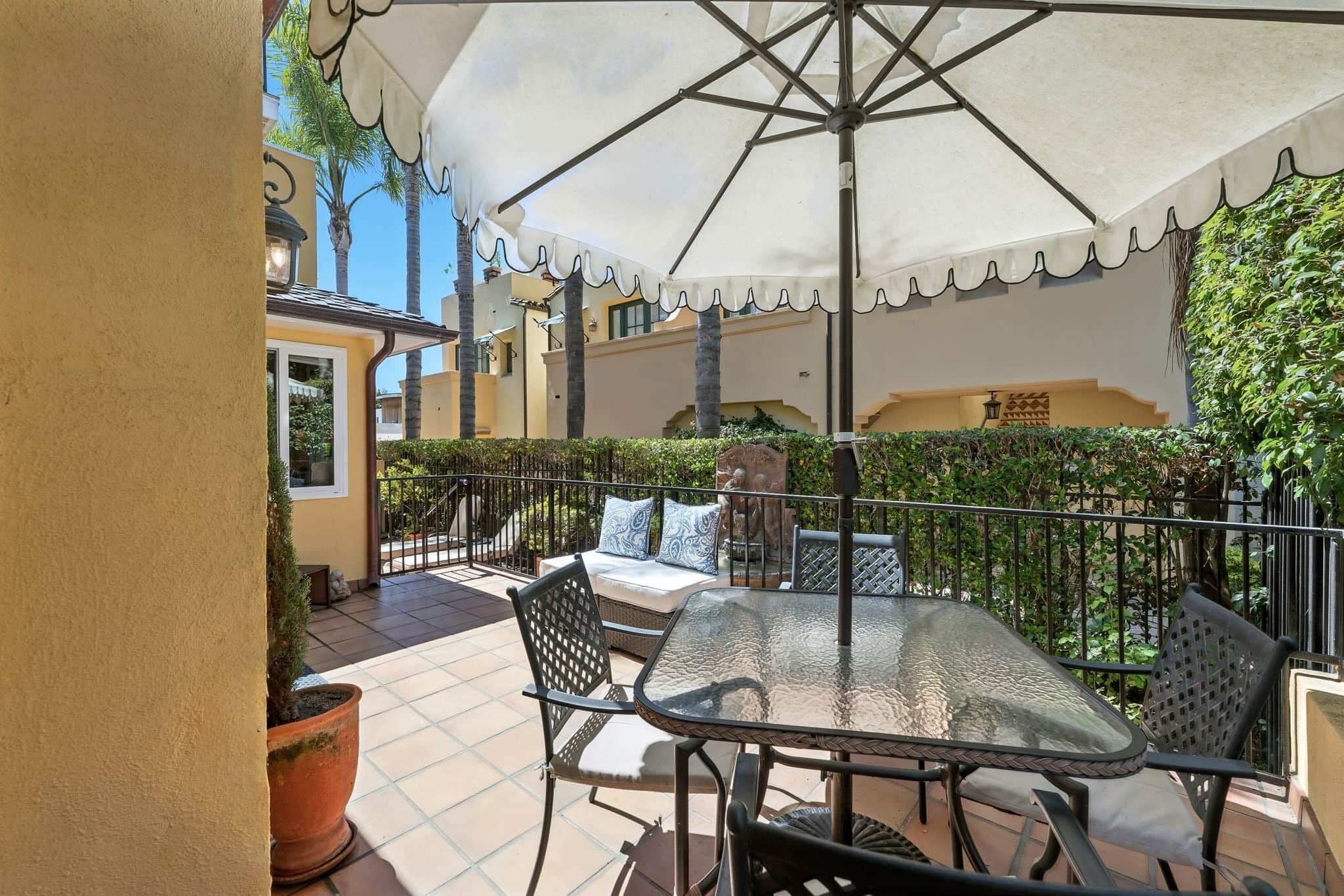 A patio with a glass table and chairs, surrounded by a white umbrella, and a view of a building with a balcony.