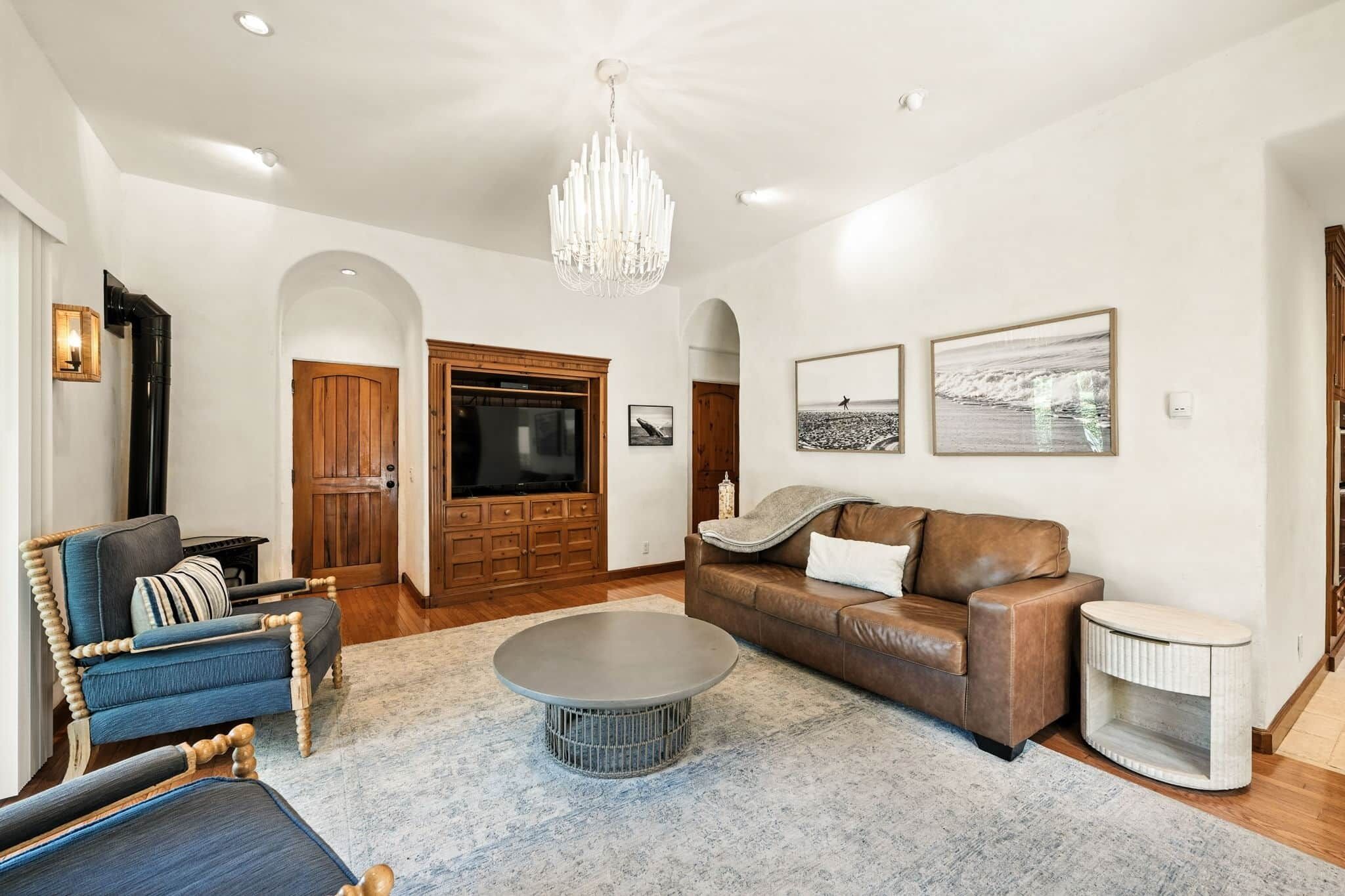 A spacious living room with a large chandelier, a brown leather sofa, a blue armchair, and a round coffee table.