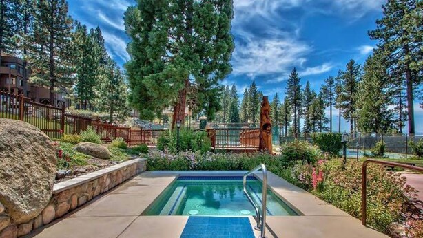 A swimming pool with a wooden deck, surrounded by a stone wall and a metal fence.