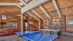 A spacious room with a ping pong table, red chairs, and a kitchen area.