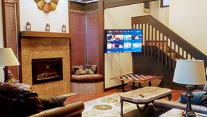 A cozy living room with a fireplace, a television, and a staircase.