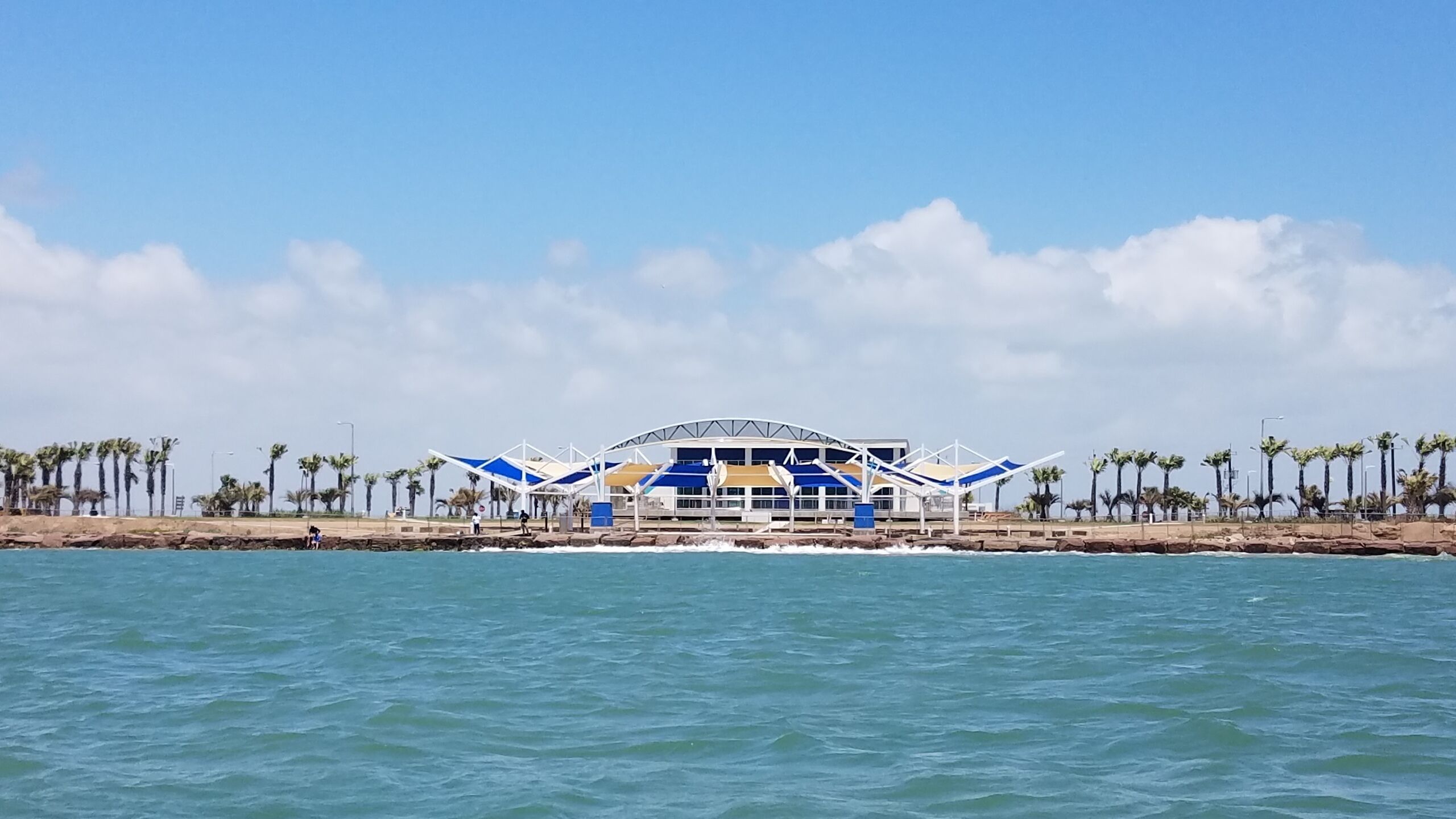 A coastal view with a large, modern building with a blue and white color scheme, located near the water.