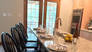Une cuisine dotée d’un îlot central, d’un coin repas avec des chaises et d’une vue sur l’extérieur grâce à une porte vitrée.