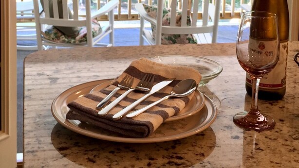 Un coin repas avec une table dressée pour deux personnes, une bouteille de vin et un verre posé sur le comptoir.
