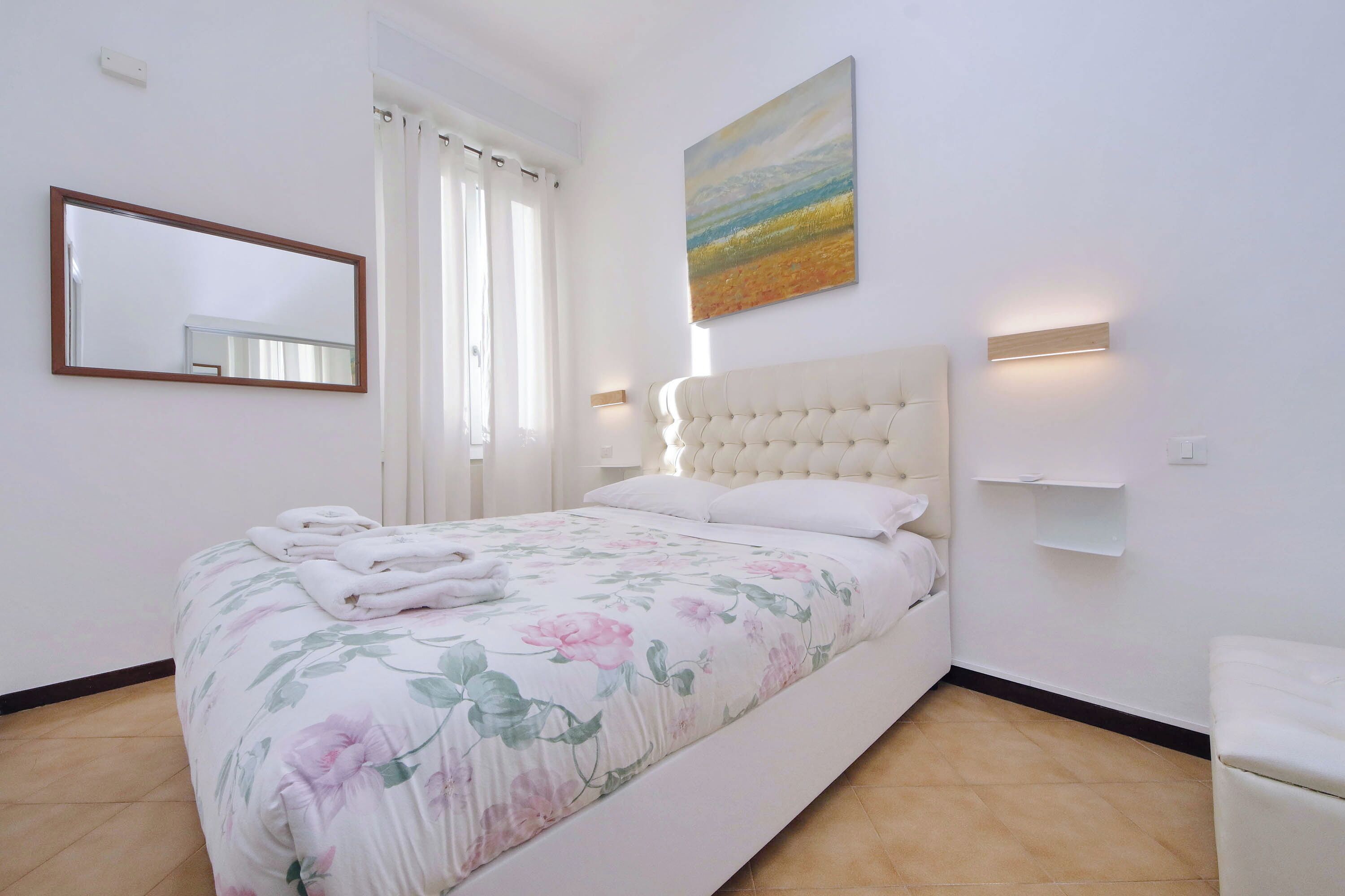 Ein Schlafzimmer mit Bett, Spiegel, Gemälde und Nachttisch.