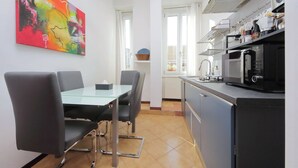 Een moderne keuken met een eethoek, met een glazen tafel, zwarte stoelen en een kleurrijk abstract schilderij aan de muur.