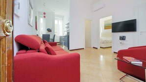 Een moderne woonkamer met rode banken, een flatscreen televisie en een keuken op de achtergrond.