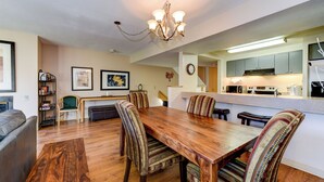 A dining area with a wooden table and striped upholstered chairs, a chandelier, and a kitchen in the background. - Amazing Views-Free shuttle, Lodge access pool/gym. (Keystone)