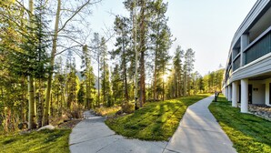 A modern building with a curved facade, a paved pathway, and a forested area. - Amazing Views-Free shuttle, Lodge access pool/gym. (Keystone)
