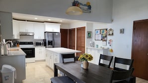 Eine moderne Küche mit weißen Schränken, einem Edelstahlkühlschrank und einem Essbereich mit Holztisch und -stühlen.