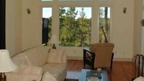 A spacious living room with a high arched ceiling, large windows offering a view of trees, and a cozy seating area with a sofa and armchairs.