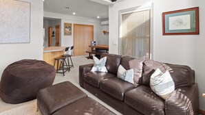 Een moderne woonkamer met een bruine leren bank, een relaxfauteuil en een eethoek met een houten tafel en stoelen.
