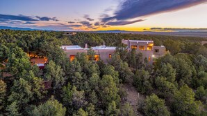Una casa moderna rodeada de un bosque frondoso, con una vista despejada del atardecer al fondo.